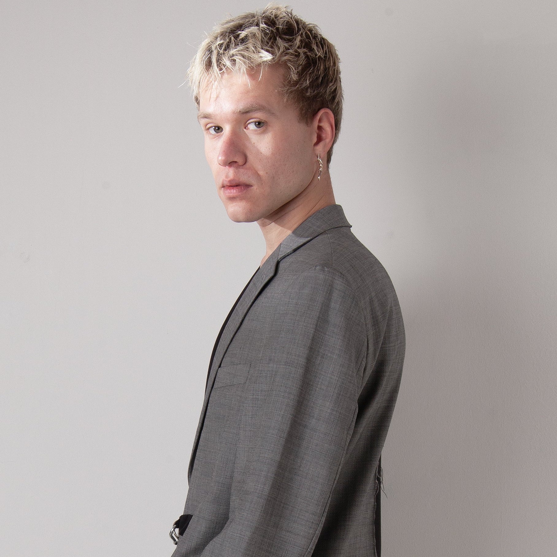 Man wearing a gray blazer and black pants with blue patterns on a plain background